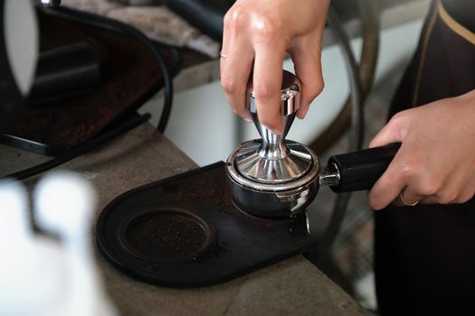 A female worker uses a tamper rod to press roasted coffee beans before they are put into the coffee machine.