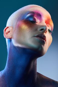 Studio shot of a young woman posing with multi-coloured paint on her face.