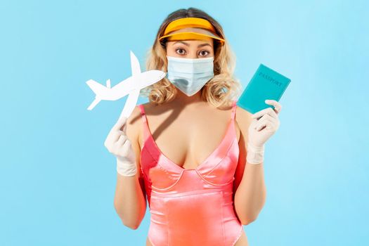 Summer trip with covid-19. Woman in swimsuit, wearing hygienic face mask and gloves to prevent contagious coronavirus, holding passport and flying airplane, dreaming of travelling, safe resort tour