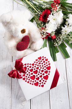 Valentine's day gift, teddy bear with a heart, a box of pralines and a bouquet of flowers on the bed early in the morning. High quality photo