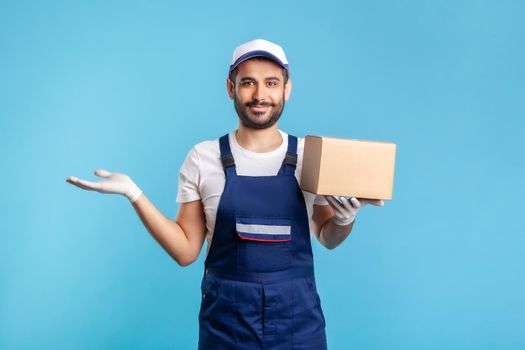 Happy worker in uniform carrying cardboard box and raising other hand to hold empty space, advertising area for commercial image. Concept of cargo transportation, delivery service, express shipping