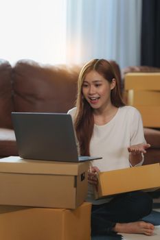 Image of Young asian woman startup freelance with parcel box and talking with customer by computer laptop. Online marketing packing box delivery concept