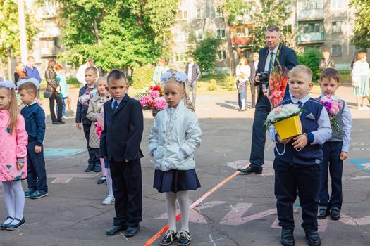 NOVOKUZNETSK, KEMEROVO REGION, RUSSIA - SEP, 1, 2021: Meeting with the first-grade pupils and teacher at schoolyard. The day of knowledge in Russia.