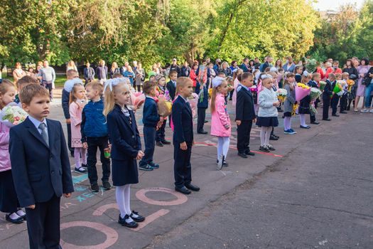 NOVOKUZNETSK, KEMEROVO REGION, RUSSIA - SEP, 1, 2021: Meeting with the first-grade pupils and teacher at schoolyard. The day of knowledge in Russia.