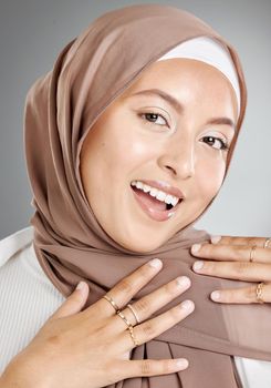 Studio portrait of beautiful and modest muslim woman isolated against a grey background. Young woman wearing a hijab or headscarf showing traditional arab modesty while smiling and looking at camera.