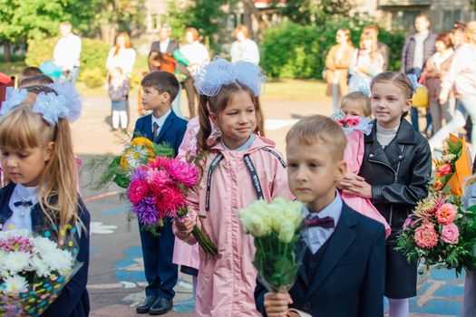 NOVOKUZNETSK, KEMEROVO REGION, RUSSIA - SEP, 1, 2021: Meeting with the first-grade pupils and teacher at schoolyard. The day of knowledge in Russia.