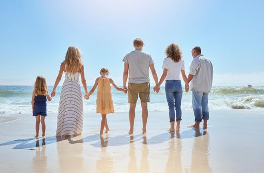 Rear view of family holding hands and having fun on a beach vacation together on a sunny day. Relatives enjoying summer and sunshine, bonding and spending quality time walking and feeling ocean water.