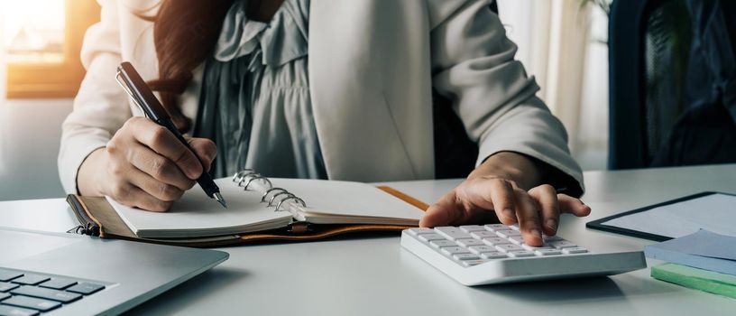 Accountant female writing information on paper while using calculator in workplace. office concept.