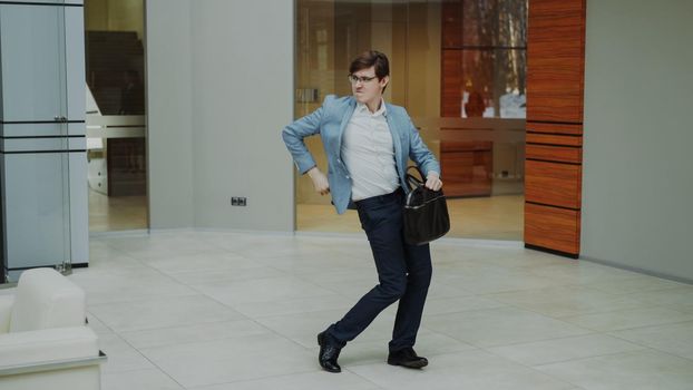 Crazy businessman dancing with briefcase in modern lobby indoors alone