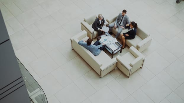 Top view of group of business people colleagues discussing financial charts sitting on couchs in lobby at modern business center indoors