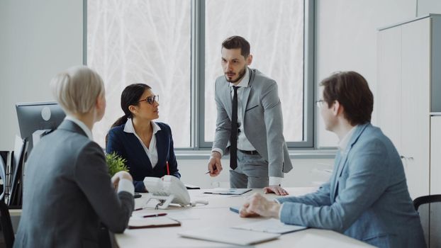 Businesswoman discussing reports with male and female colleagues sitting at the table in modern office indoors