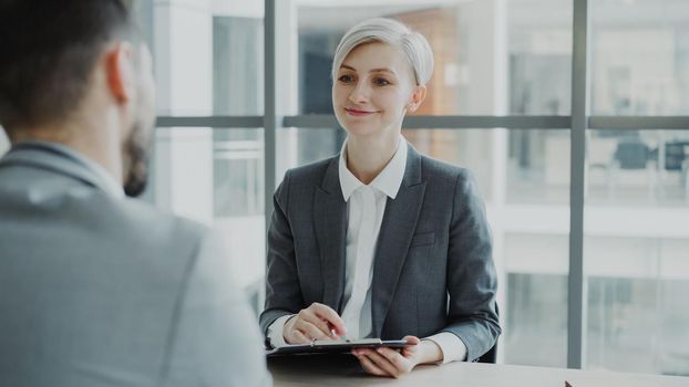 HR businesswoman having job interview with young man in suit and watching his resume application in modern office indoors