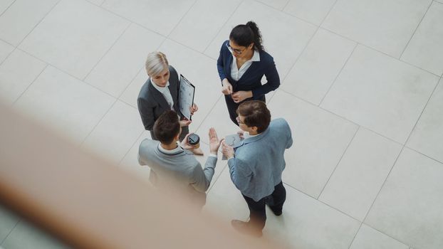 Top view of group of business people in suits discussing financial graphs in lobby of business center