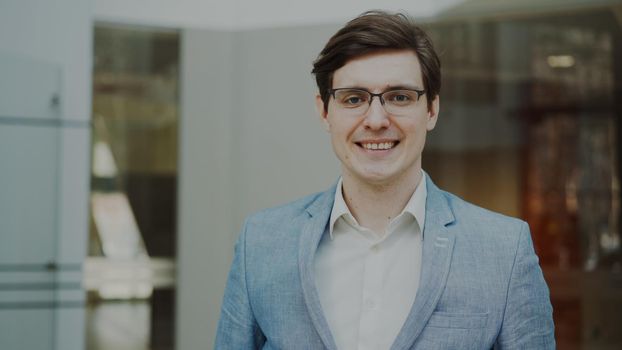 Portrait of successful smiling businessman in glasses looking into camera in modern office indoors