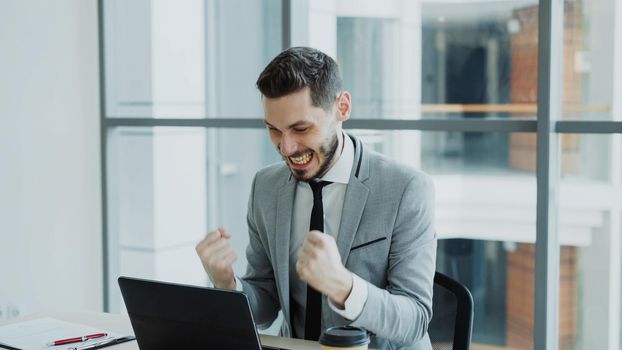 Young businessman using laptop computer receiving good message and become very excited and happy sits in modern office indoors
