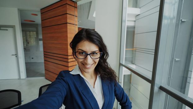 POV of young businesswoman in suit taking a selfie photo holding smartphone and have fun in modern office indoors