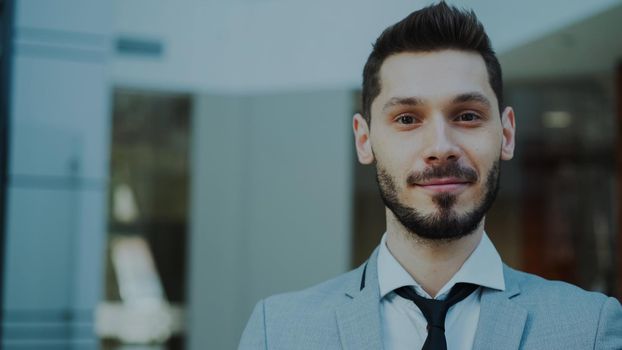 Portrait of successful young smiling businessman looking into camera in modern office indoors