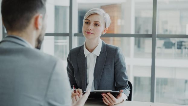 HR businesswoman having job interview with young man in suit and watching his resume application in modern office indoors