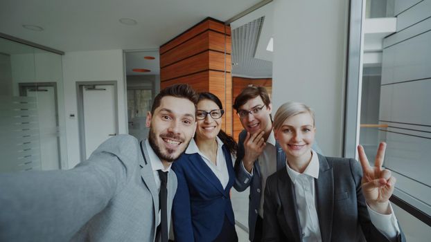 POV of Happy business team taking selfie portrait on smartphone camera and posing for group photo during meeting in modern office indoors