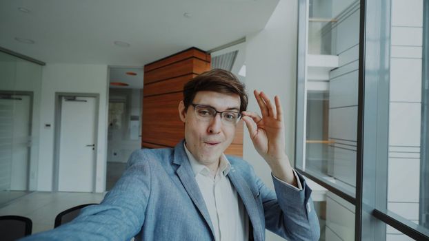 POV of young joyful businessman in glasses taking a selfie photo and have fun in modern office indoors