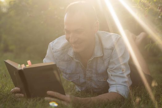 Young man lying in the grass, relaxing and reading a book.