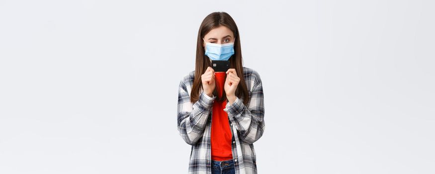 Coronavirus outbreak, working from home, online shopping and contactless payment concept. Cheerful pretty woman in medical mask showing credit card and wink sassy.