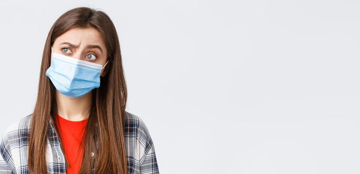 Coronavirus outbreak, leisure on quarantine, social distancing and emotions concept. Thoughtful and intrigued woman in medical mask, looking left with interest, thinking, white background.