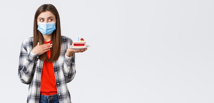 Coronavirus outbreak, lifestyle during social distancing and holidays celebration concept. Dreamy happy young girl in medical mask celebrating birthday, hold b-day cake, think what wish.