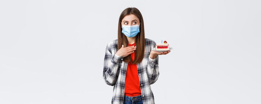 Coronavirus outbreak, lifestyle during social distancing and holidays celebration concept. Dreamy happy young girl in medical mask celebrating birthday, hold b-day cake, think what wish.