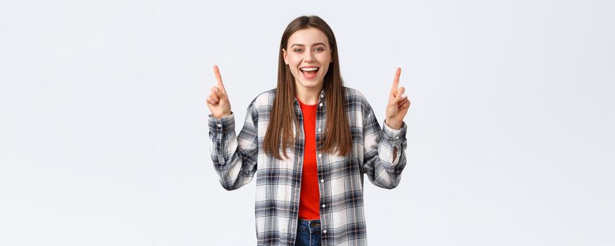 Lifestyle, different emotions, leisure activities concept. Happy beautiful girl in checked shirt, pointing fingers up and laughing carefree, showing good summer vacation ideas, promo or banner.