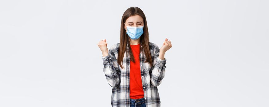 Different emotions, covid-19 pandemic, coronavirus self-quarantine and social distancing concept. Satisfied happy young woman in medical mask, fist pump in celebration victory, success achieved.