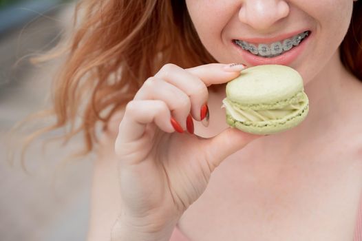 Young red-haired woman with braces eating macaron cake