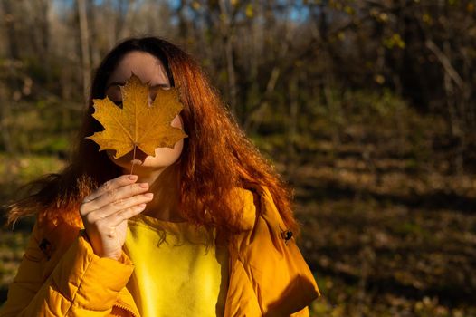 Red-haired Caucasian woman holding a fallen maple leaf. Autumn Walk