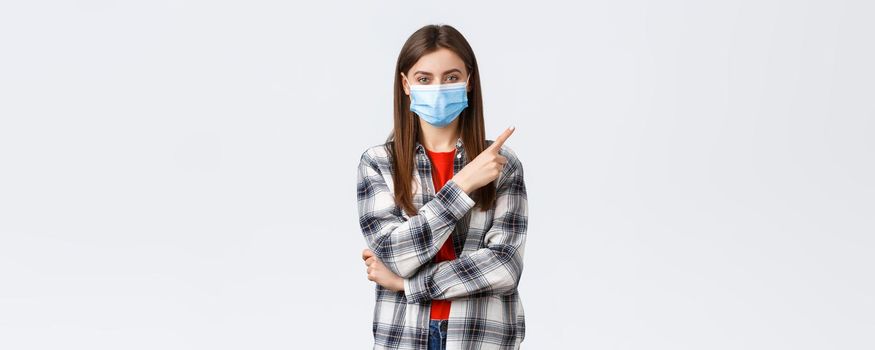 Coronavirus outbreak, leisure on quarantine, social distancing and emotions concept. Happy smiling young woman in medical mask provide information on covid-19 pointing finger upper right.