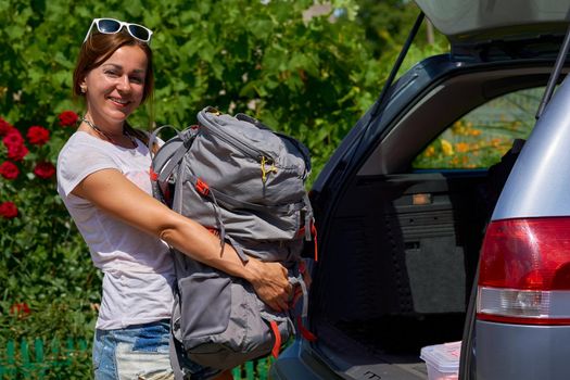 a journey for pleasure in which several different places are visited. A young woman puts a backpack and other things in the car going on a tour. High quality photo