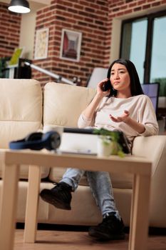 Authentic smiling woman talking on phone in her living room flat apartment, young asian woman mobile business phone call relaxing lifestyle internet communication connection