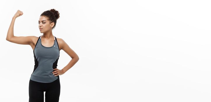 Healthy and Fitness concept - Portrait of young beautiful African American showing her strong muscle with confident cheerful facial expression. Isolated on white studio background