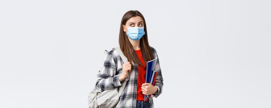 Coronavirus pandemic, covid-19 education, and back to school concept. Smart female student, freshman girl heading to class, look upper left corner interested at banner, hold notebooks and backpack.