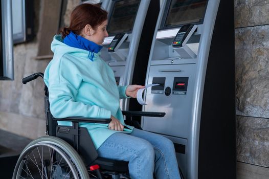 Caucasian woman in a wheelchair buys a ticket at a self-service ticket office