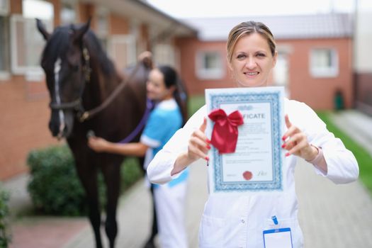 Woman veterinarian holds medical certificate on background of horse. Thoroughbred sport horses and passport concept