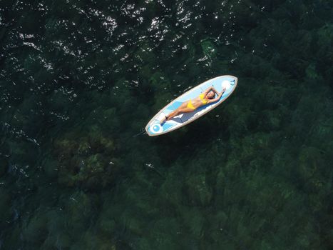 Side view foto of a woman sitting and relaxing on the sup board. Young attractive woman in the sea on the Stand Up Paddle Board SUP. The concept of an active and healthy life in harmony with nature.