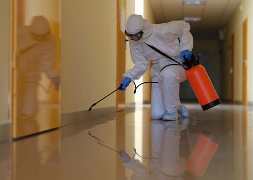 Person in protective suit disinfects office and corridors to prevent spread of COVID-19. Disinfection of premises in medical institutions concept