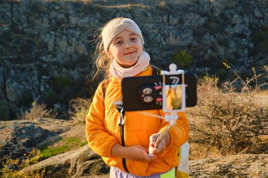 Shot of a kid girl talking on camera in hills, make video blog use device make video hold hand social network blog. child vlogger filming video diary outdoors. kid creating social media content.