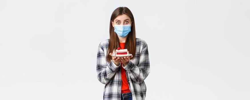 Coronavirus outbreak, lifestyle during social distancing and holidays celebration concept. Enthusiastic cute girl in medical mask, holding delicious cake, make home delivery from cafe.