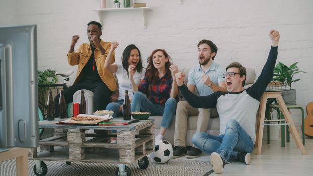 Group of happy friends watching sports game on TV at home indoors. They are happy about their favorite team win competition