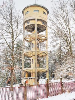 Water tower in a snowy forest park at field against a cloudy sky. Historical technical architecture at hill peak.
