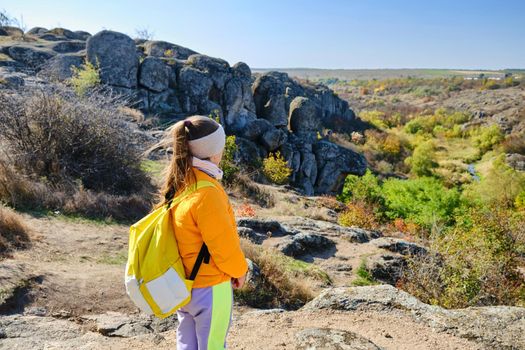 little girl with a yellow backpack standing on a mountain top at the day time