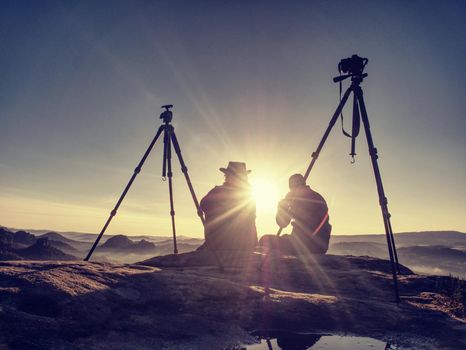 Couple tourists with tripods and cameras take pictures to the background of beautiful hills and sky. Young people in a mountain hike. Freedom and travel concept.