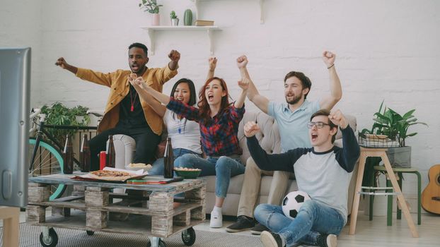 Group of happy friends watching sports game on TV at home indoors. They are happy about their favorite team win competition