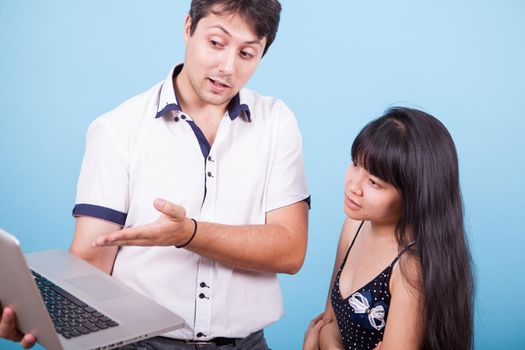 Cacausian male showing his asian girlfriend something on his computer in studio. Caucasian male married with asian female.